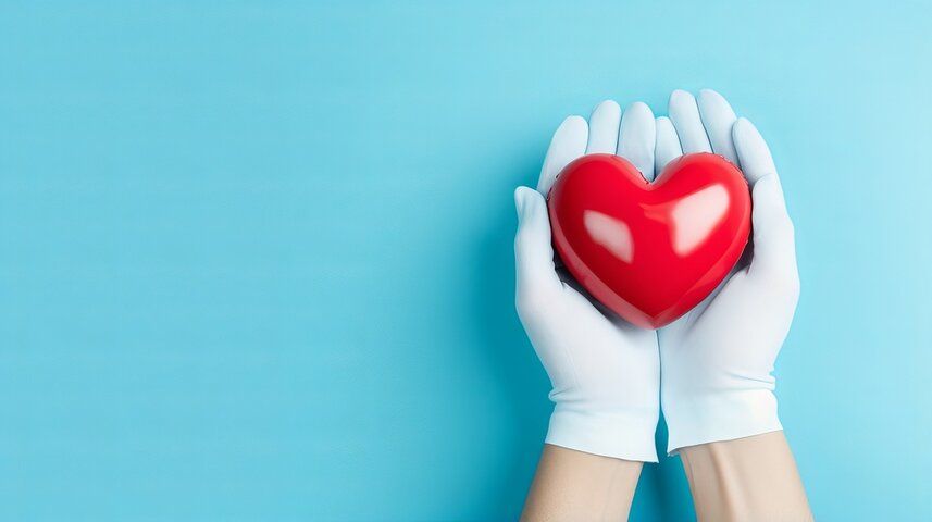A doctor's gloved hands are holding a rubber heart.